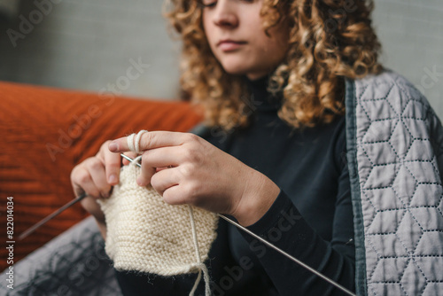 Pretty young woman teaching herself knitting skills, sitting on floor, girl looking attentively. Handicraft