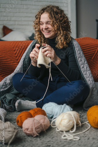 Curly haired woman knitting with needles using wool yarn creating clothes from hard work. Young woman knitting thread.