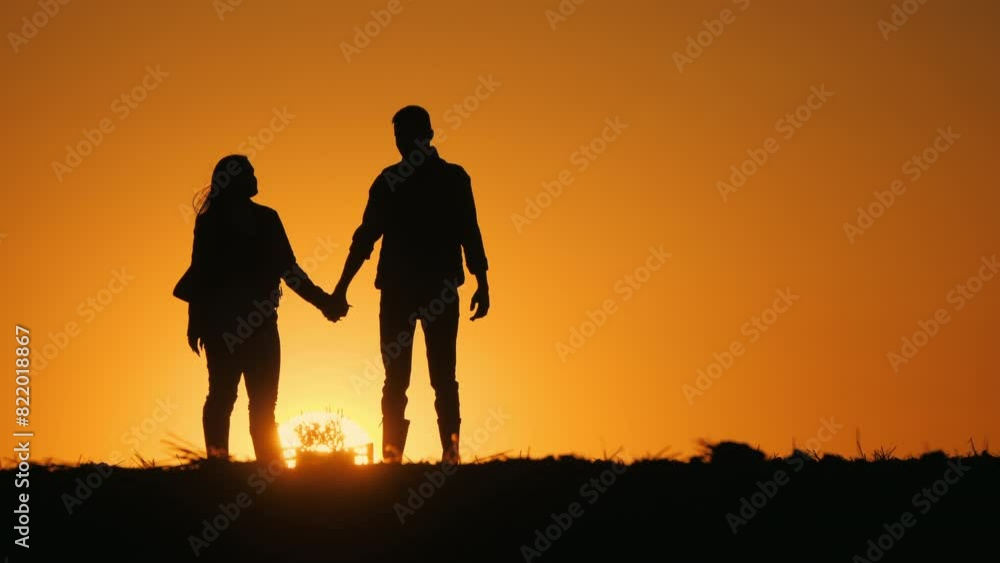 Silhouettes of a young couple holding hands and looking forward at a beautiful sunset Silhouettes of a young couple holding hands and looking forward at a beautiful sunset