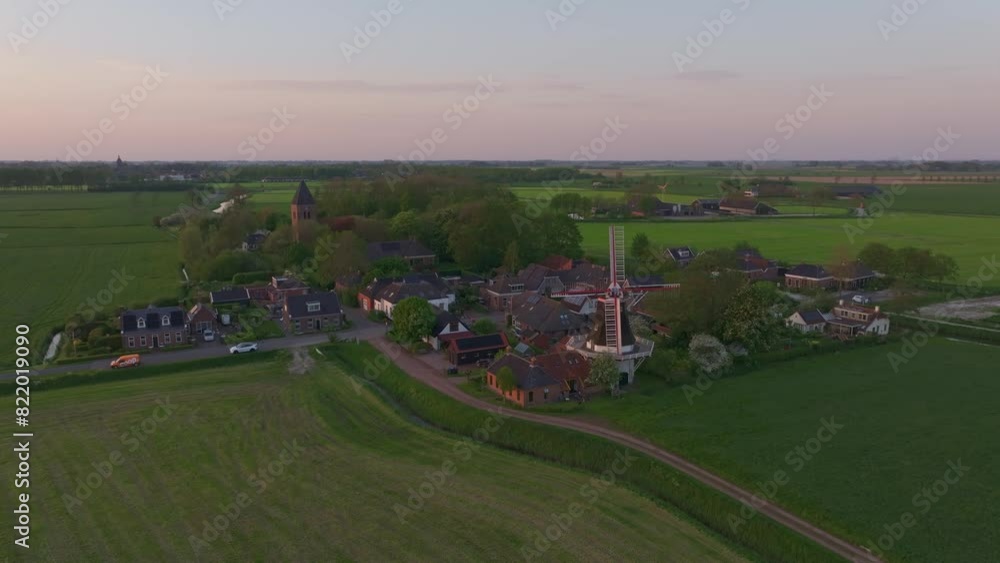 Aerial view of peaceful village with windmill and church at sunset, Westerwijtwerd, Netherlands.