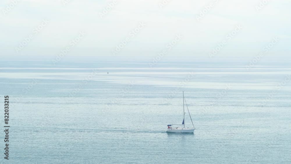 Sailboat sailing peacefully through the calm waters of the sea on a cloudy day. Sailboat sailing peacefully through the calm waters of the sea on a cloudy day.