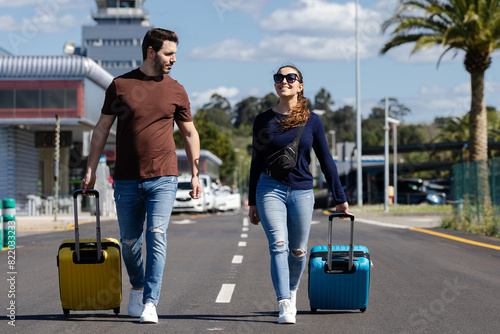 Couple leaving the airport with their suitcases. Couple on honeymoon in their favorite city. Couple in love starting their vacation. Young people leaving the airport to visit their family or friends.