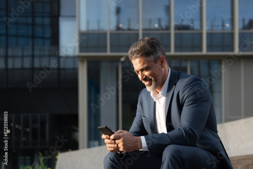 Confident middle age male entrepreneur businessman in formal suit working on mobile cell phone at office. Successful 40s mature hispanic senior business man using smartphone cellphone financial app