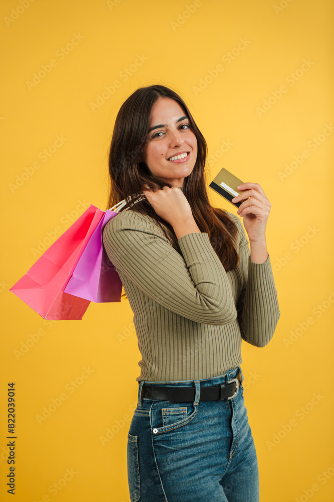 © Jose Calsina - Vertical portrait of a young caucasian customer woman holding shopping bags and a credit card, contemplating whether to buy clothes from an online store. She is against a yellow background purchasing © Jose Calsina - Vertical portrait of a young caucasian customer woman holding shopping bags and a credit card, contemplating whether to buy clothes from an online store. She is against a yellow background purchasing