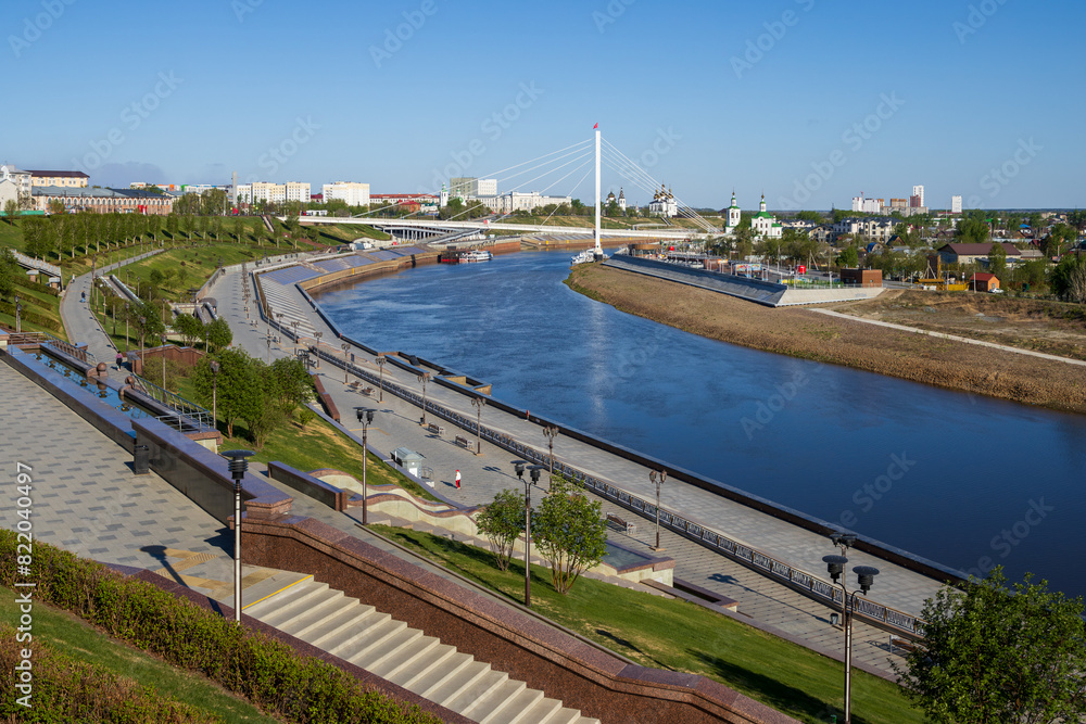 Tyumen city, Tyumen region, Siberia, Russia. Beautiful view of the Tura River, cable-stayed pedestrian bridge and churches in the historical center of the city. Landscaped river embankment. Tyumen city, Tyumen region, Siberia, Russia. Beautiful view of the Tura River, cable-stayed pedestrian bridge and churches in the historical center of the city. Landscaped river embankment.