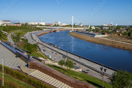 Tyumen city, Tyumen region, Siberia, Russia. Beautiful view of the Tura River, cable-stayed pedestrian bridge and churches in the historical center of the city. Landscaped river embankment. photo