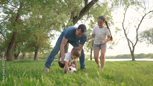 family playing football. people parks and nature concept. young father with his daughter and son playing with a soccer ball in nature, running on the grass and lifestyle laughing