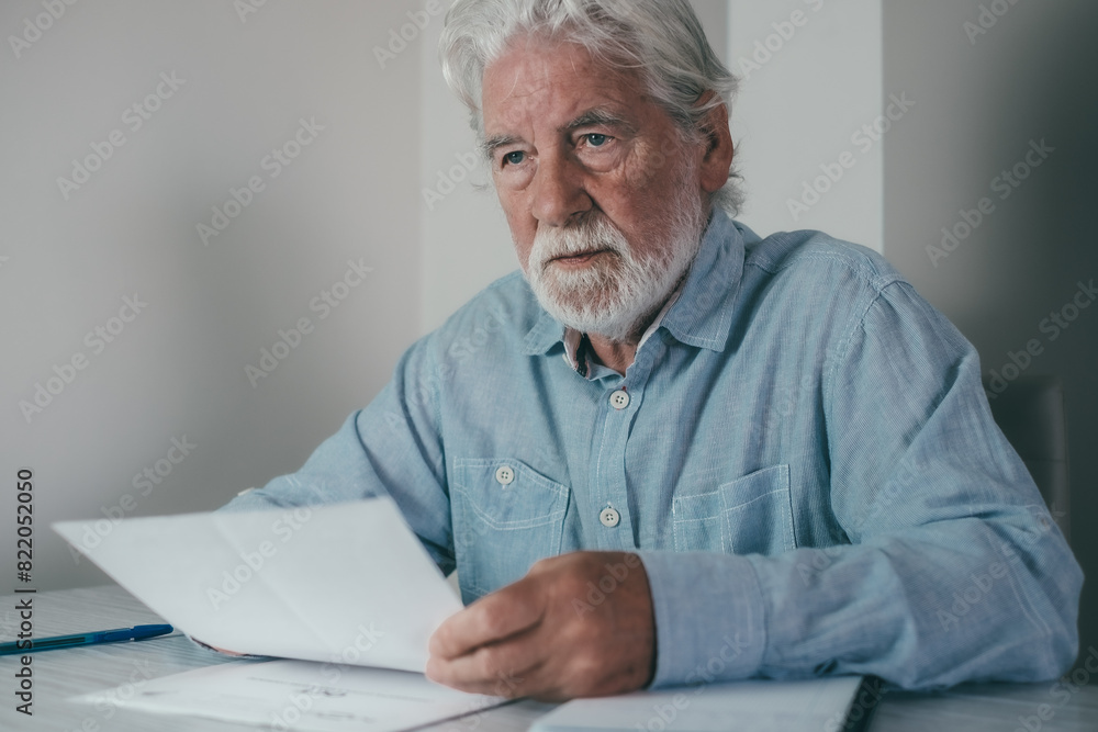 Senior bearded financial advisor man consulting documents sitting indoor at home or school classroom holding papers talking with student, client, investor Senior bearded financial advisor man consulting documents sitting indoor at home or school classroom holding papers talking with student, client, investor