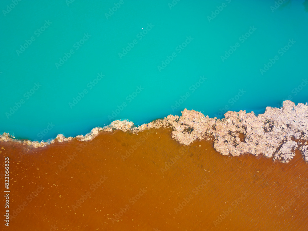 Aerial drone view of polluted river. The aftermath of excessive phosphate release to the river. Turquoise and brown colors. Environmental disaster caused by humans. Ecological concern.