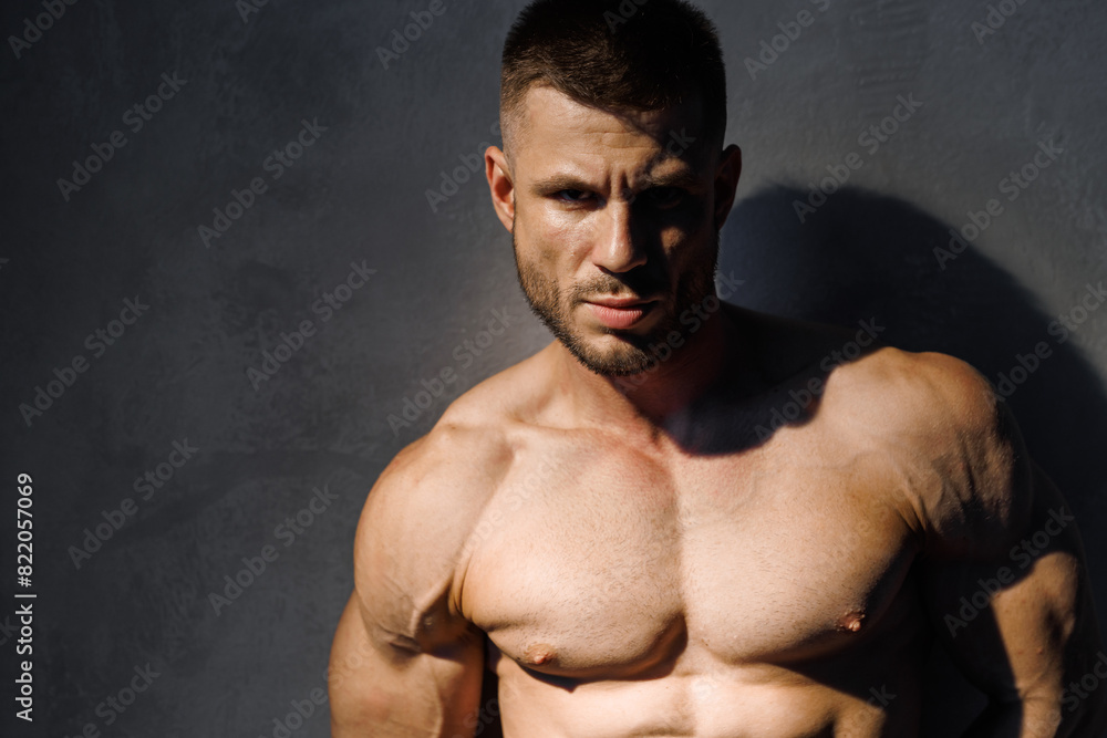Fototapeta premium Muscular model sports young man on dark background. Fashion portrait of strong brutal guy. Male flexing his muscles.