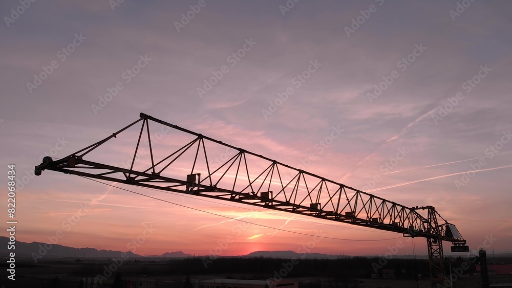 Close up during colorful sunset of Tower crane, big excavator silhouette in a construction site. Aerial drone view Close up during colorful sunset of Tower crane, big excavator silhouette in a construction site. Aerial drone view