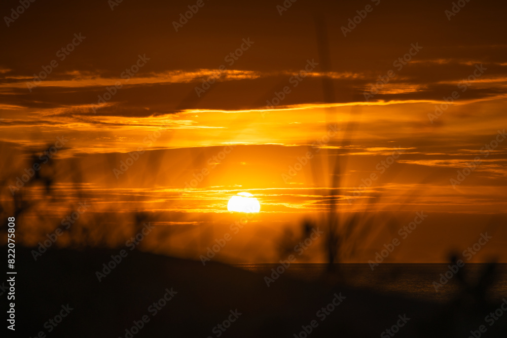a sunset from the grass in the dunes, dark clouds above a sunset from the grass in the dunes, dark clouds above