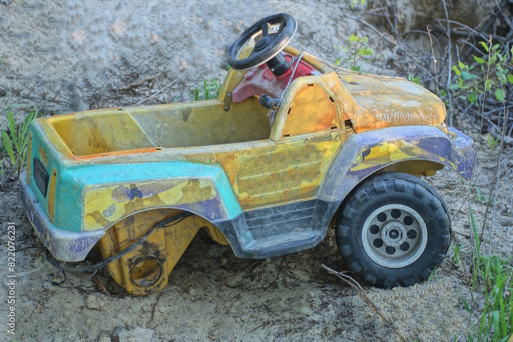one large broken plastic colored toy car stands on gray sand on the street