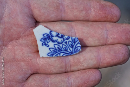 hand holding a piece of white small old ceramic tile with blue pattern on the street