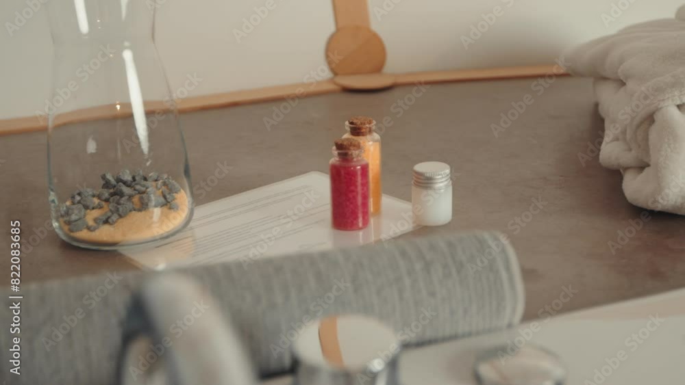 Close-up of glass jar with rocks and sand, small bottles, and towels on a countertop. Spa and relaxation setting Close-up of glass jar with rocks and sand, small bottles, and towels on a countertop. Spa and relaxation setting