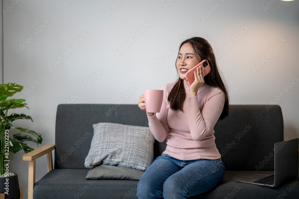 A woman is sitting on a couch and talking on her cell phone. She is holding a pink mug and a laptop A woman is sitting on a couch and talking on her cell phone. She is holding a pink mug and a laptop
