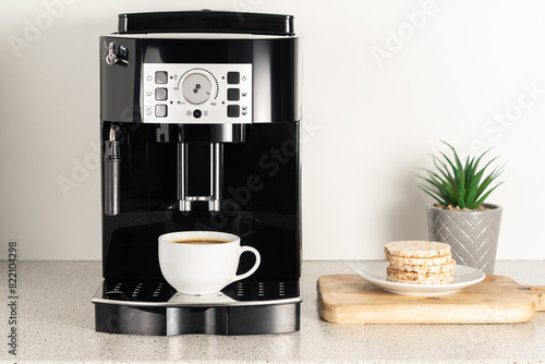 Modern espresso coffee machine with a cup in interior of kitchen closeup.