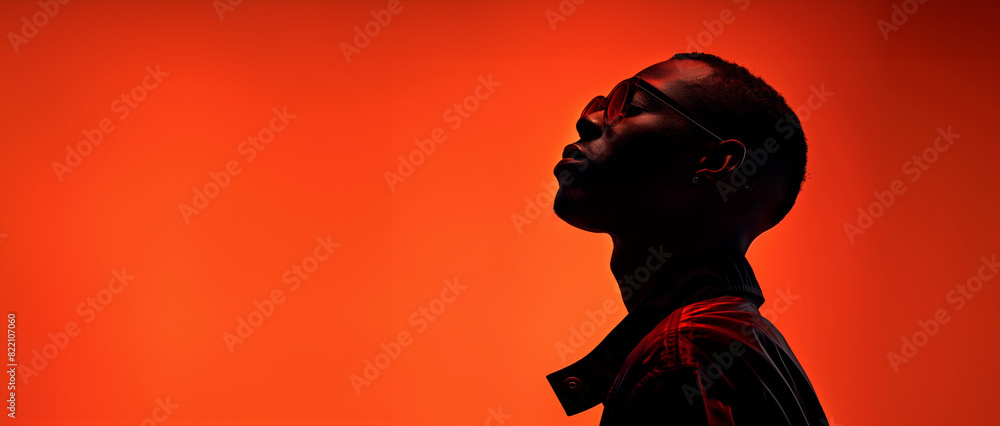 A man in a black jacket stands in a red background. Futuristic silhouette of a guy wearing high-end fashion, the guy is just slightly visible due to dark shadows, he is wearing modern fashion frames A man in a black jacket stands in a red background. Futuristic silhouette of a guy wearing high-end fashion, the guy is just slightly visible due to dark shadows, he is wearing modern fashion frames