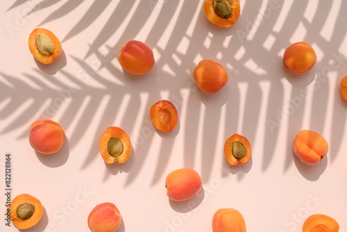 Apricot fruit with palm leaves shadow on a pastel pink background. Summer aesthetic concept.