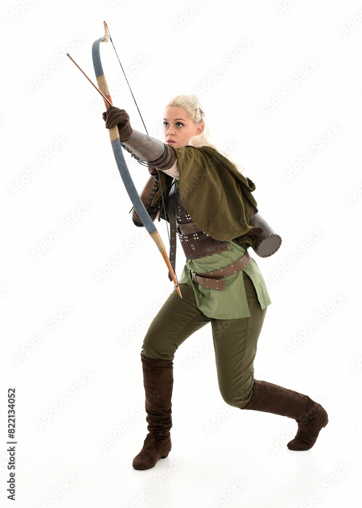 full length portrait of blonde female model wearing green fantasy elf warrior halloween costume with leather armour. standing pose, holding weapons. isolated on white studio background. full length portrait of blonde female model wearing green fantasy elf warrior halloween costume with leather armour. standing pose, holding weapons. isolated on white studio background.