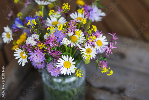 Wildflowers in a glass vase on rustic wooden table in summer - garden feeling, summertime concept
