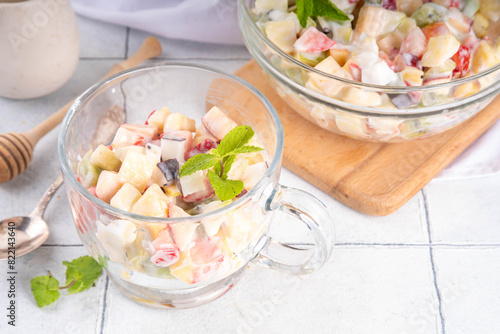 Creamy summer fruit salad with apples, pineapple, kiwi, peaches, strawberry, bananas, honey and greek yogurt sauce. Healthy summer diet food recipe, on white kitchen table copy space