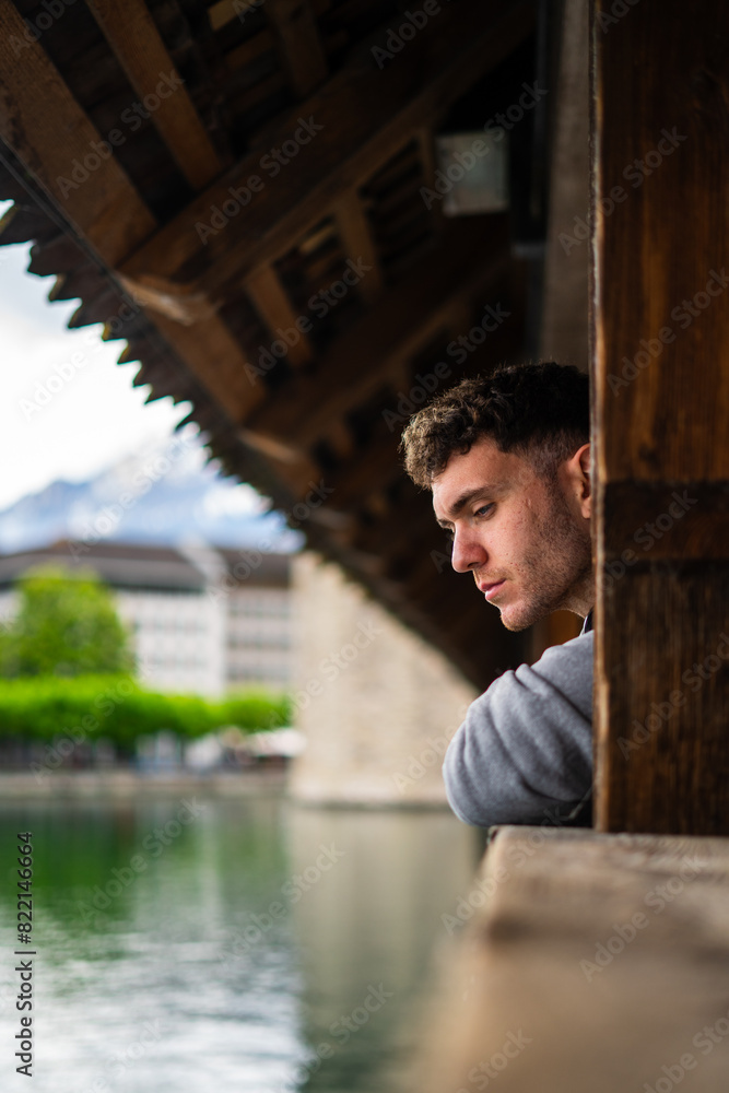 Fototapeta premium Side view of handsome young man leaning on bridge while thinking about life. Lucerne. Chapel bridge