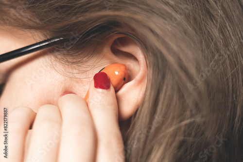 Woman is insert  into the ear Orange Wireless Bluetooth Earphones. Modern Stereo Earplugs, Sports Headset.