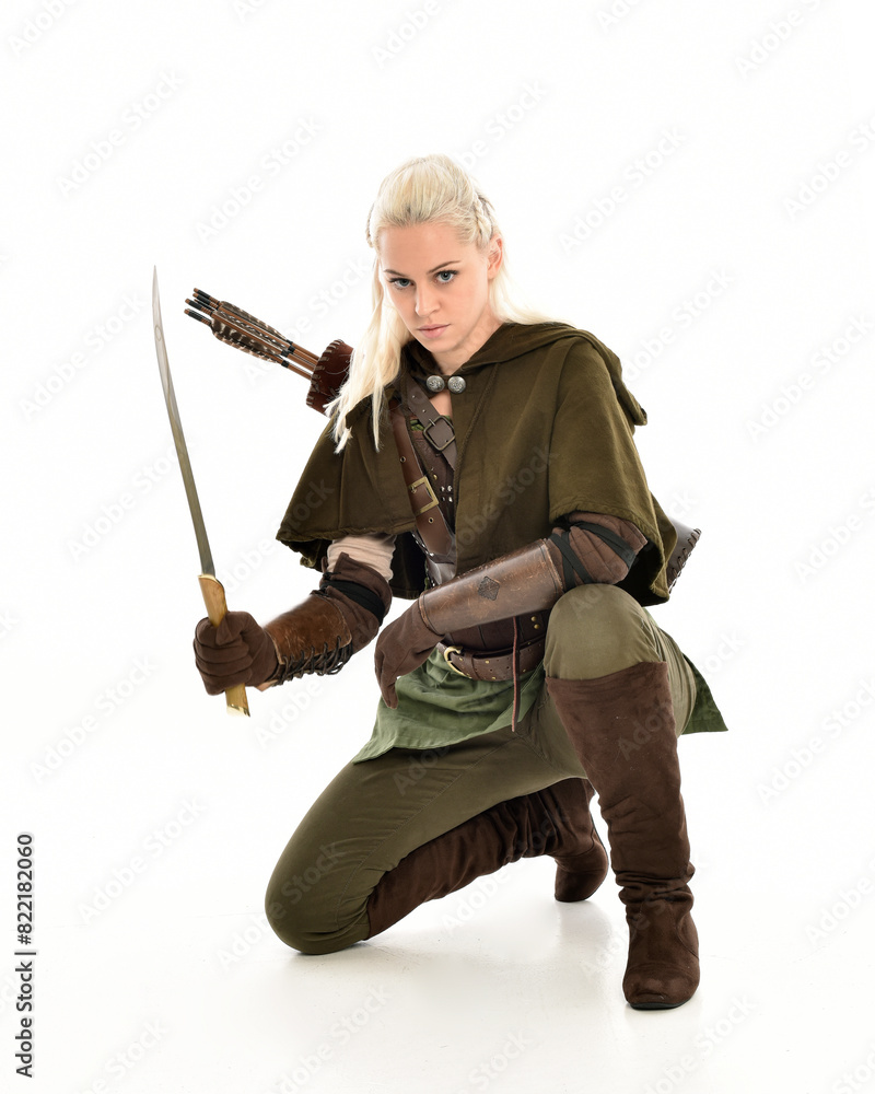 full length portrait of blonde female model wearing green fantasy elf warrior halloween costume with leather armour. sitting pose kneeling. isolated on white studio background. full length portrait of blonde female model wearing green fantasy elf warrior halloween costume with leather armour. sitting pose kneeling. isolated on white studio background.