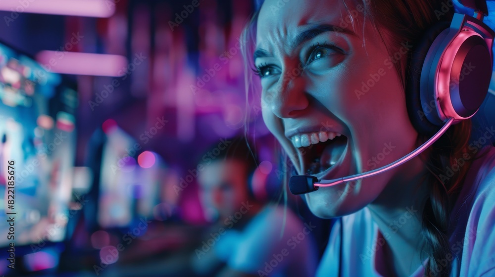 Fototapeta premium A young female gamer playing on a computer. She is wearing headphones and taking part in the PvP tournament. She is wearing earphones and talking with the team over a microphone.