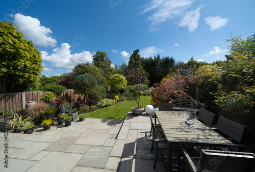 Beautiful summer garden in England, UK with lawn, table and chairs and large indian sandstone patio.