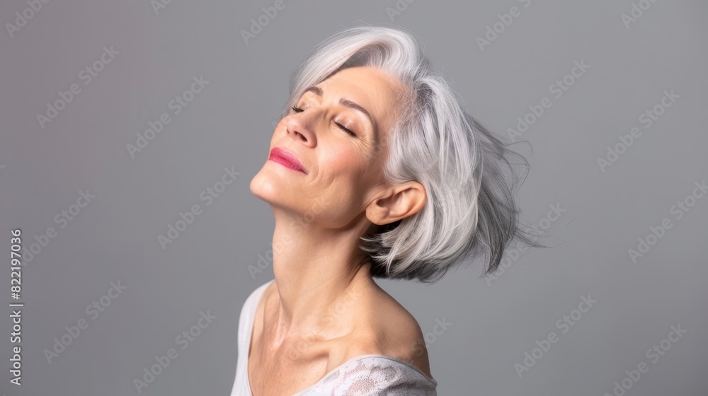 Elegant elderly woman with short white hair, eyes closed, and a peaceful expression, wearing a white top against a grey background. Elegant elderly woman with short white hair, eyes closed, and a peaceful expression, wearing a white top against a grey background.