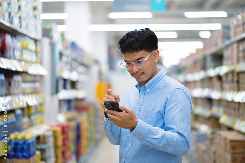 A man is looking at his cell phone in a store. He is wearing glasses and a blue shirt A man is looking at his cell phone in a store. He is wearing glasses and a blue shirt