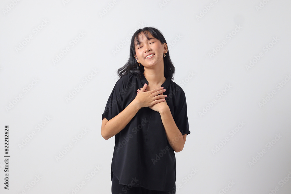 Portrait of attractive Asian woman in casual shirt placing hand on chest and feeling peaceful. Mental health day concept, expresses sympathy and love, smiles positively. Isolated on white background Portrait of attractive Asian woman in casual shirt placing hand on chest and feeling peaceful. Mental health day concept, expresses sympathy and love, smiles positively. Isolated on white background