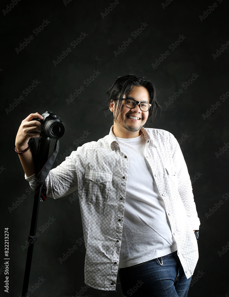 portrait of a photographer smiling happily and posing with his digital camera on a dark background portrait of a photographer smiling happily and posing with his digital camera on a dark background