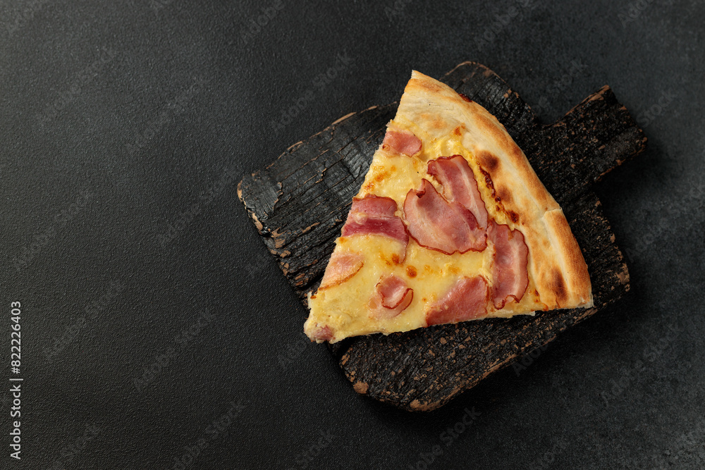 Piece of Pizza Carbonara on a black cutting board. Black background. Space for text Piece of Pizza Carbonara on a black cutting board. Black background. Space for text