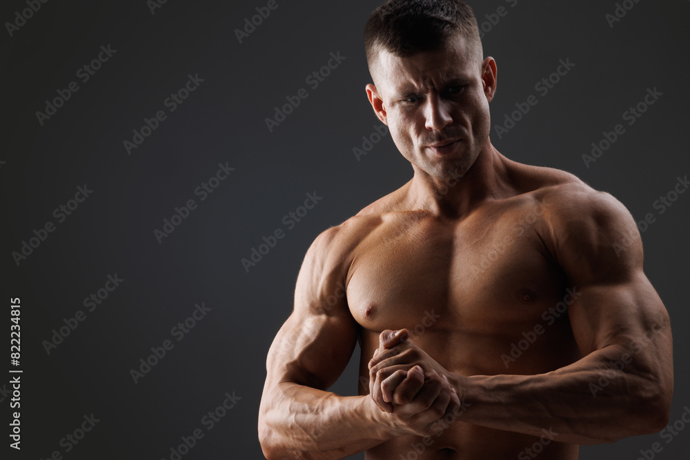 Fototapeta premium Muscular model sports young man on dark background. Fashion portrait of strong brutal guy. Male flexing his muscles.