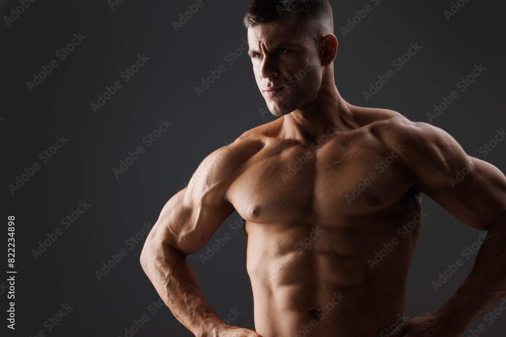 Muscular model sports young man on dark background. Fashion portrait of strong brutal guy. Male flexing his muscles.