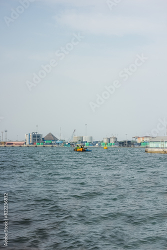 Expansive harbor view featuring a busy cityscape skyline across the water, with a small boat navigating the rippling waves in the foreground. This dynamic urban maritime scene captures the interplay o © AbiezaReswara