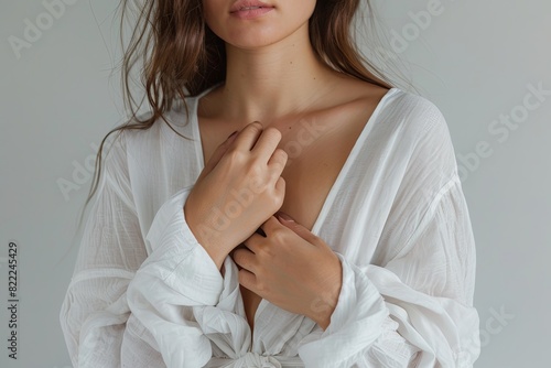 Close-up of woman in white long sleeve with hands on chest against grey background for visual contrast.