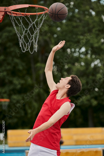 A young man in a vibrant red shirt dribbles a basketball skillfully on an outdoor court on a sunny summer day. © LIGHTFIELD STUDIOS