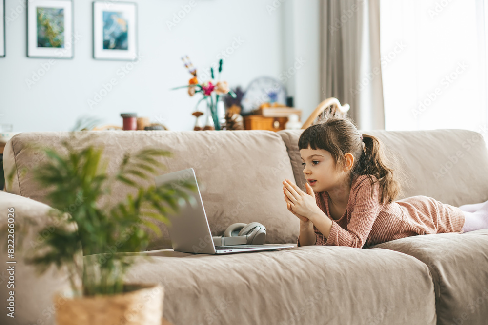Resting on a comfortable sofa, a young girl, watching a laptop, her attention fixed on the screen. Concept: technology-infused relaxation, online education, technological entertainment Resting on a comfortable sofa, a young girl, watching a laptop, her attention fixed on the screen. Concept: technology-infused relaxation, online education, technological entertainment