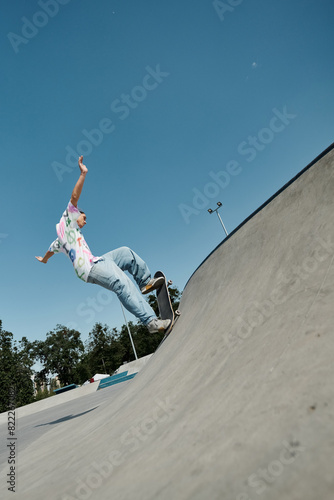 A young skater boy defies gravity as he rides his skateboard up the side of a ramp in a sunny outdoor skate park.