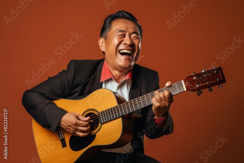 Portrait of a satisfied asian man in his 50s playing the guitar in front of blank studio backdrop