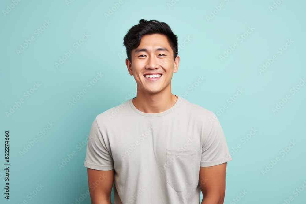 Portrait of a cheerful asian man in his 20s smiling at the camera in front of blank studio backdrop Portrait of a cheerful asian man in his 20s smiling at the camera in front of blank studio backdrop