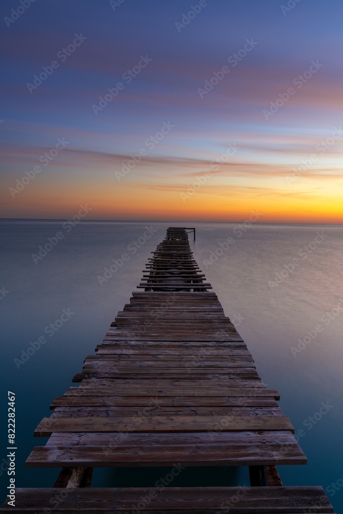 sunrise seascape with an old wooden dock leading out into the calm ocean waters sunrise seascape with an old wooden dock leading out into the calm ocean waters