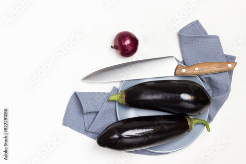 Two whole eggplants on gray plate on gray napkin. Kitchen knife on table