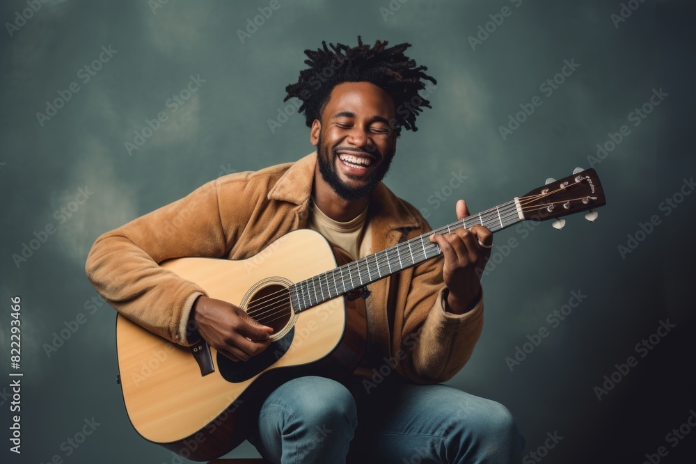 Obraz premium Portrait of a smiling afro-american man in his 20s playing the guitar in front of light wood minimalistic setup
