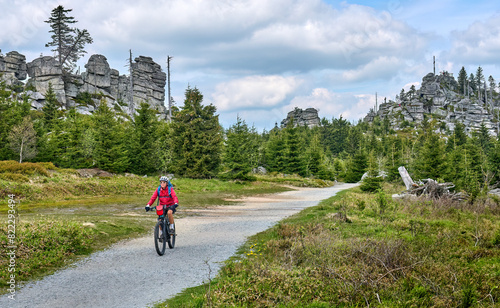 active senior woman on a bike packing tour with her electric mountain bike in the rocky the summit of Great Arber in the Bavarian Forest, Bavaria, Germany