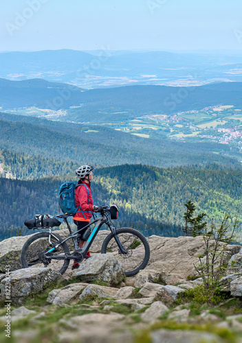 active senior woman on a bike packing tour with her electric mountain bike in the rocky  the summit of Great Arber in the Bavarian Forest, Bavaria, Germany